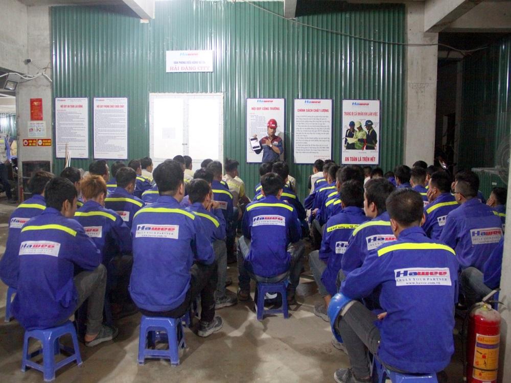 Một kỹ sư giám sát công nhân đang thi công cơ điện M&E, nhấn mạnh các tiêu chuẩn an toàn với biển báo và thiết bị bảo hộ đầy đủ trên công trường.